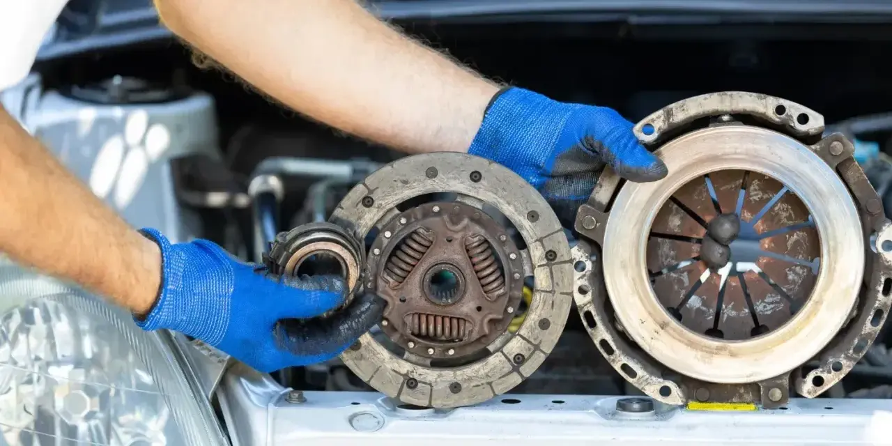Mechanik w niebieskich rękawiczkach trzyma części sprzęgła. Zastanawiasz się, ile trwa wymiana sprzęgła?