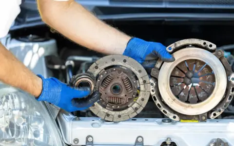 Mechanik w niebieskich rękawiczkach trzyma części sprzęgła. Zastanawiasz się, ile trwa wymiana sprzęgła?