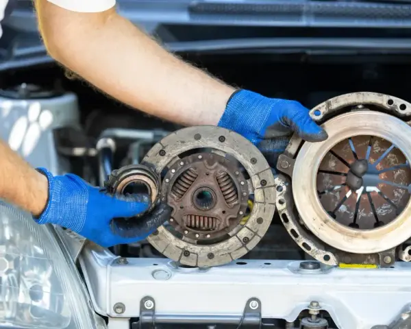 Mechanik w niebieskich rękawiczkach trzyma części sprzęgła. Zastanawiasz się, ile trwa wymiana sprzęgła?