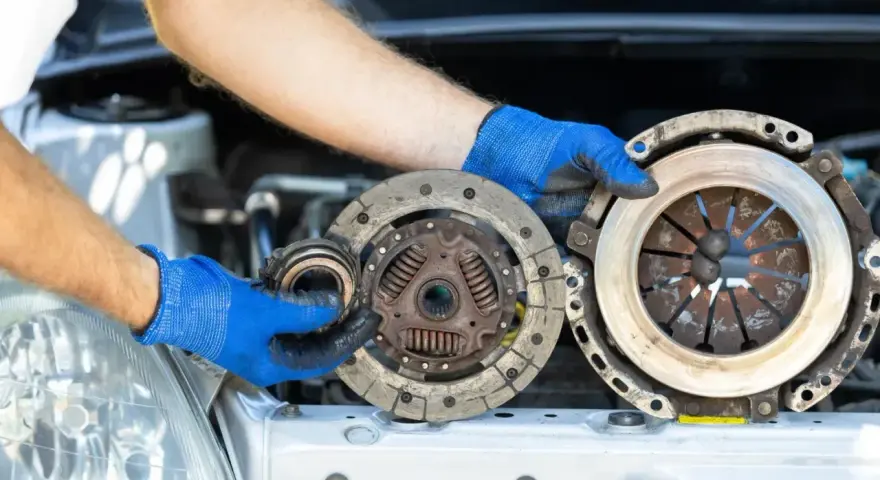Mechanik w niebieskich rękawiczkach trzyma części sprzęgła. Zastanawiasz się, ile trwa wymiana sprzęgła?