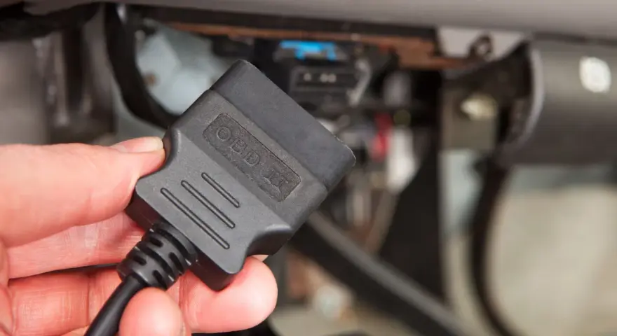 Dłoń trzyma adapter OBD II, gotowy do podłączenia i sprawdzenia kodu błędu w samochodzie.