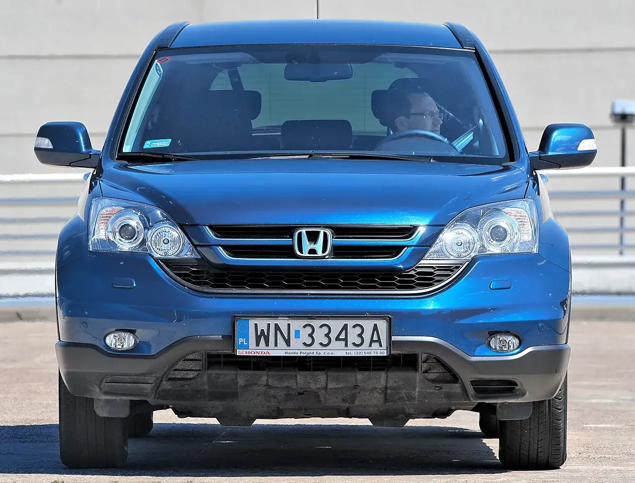 Niebieski SUV Honda CR-V z kierowcą. Czy to awd vs 4wd? Zbliżenie na prz&oacute;d auta z polskimi tablicami.