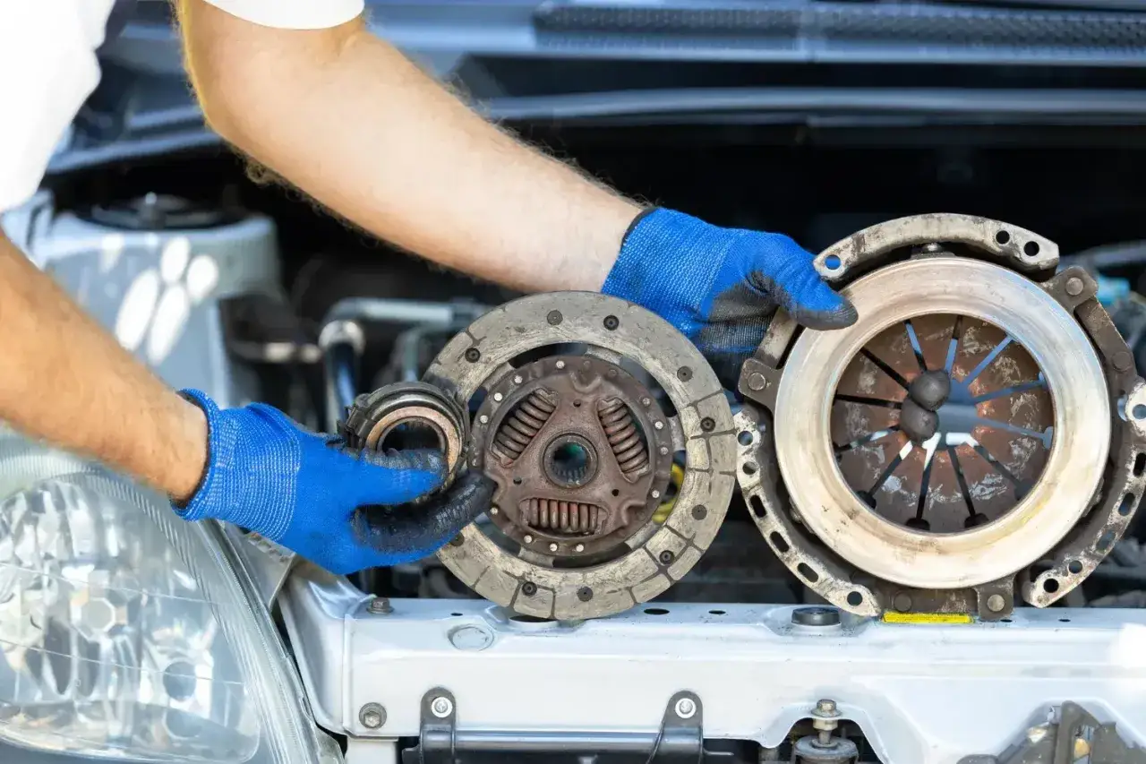 Mechanik w niebieskich rękawiczkach trzyma zużyte części sprzęgła. Zastanawiasz się, ile trwa wymiana sprzęgła?